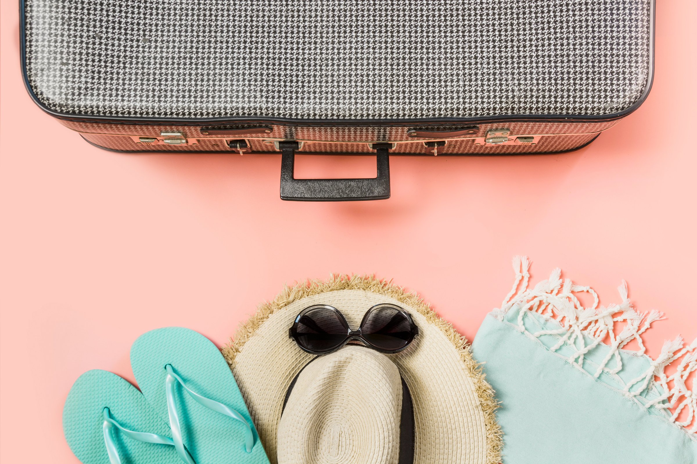 Suitcase with female outfit for beach on pink. Top view with copy space. Summer tropical vacatons.